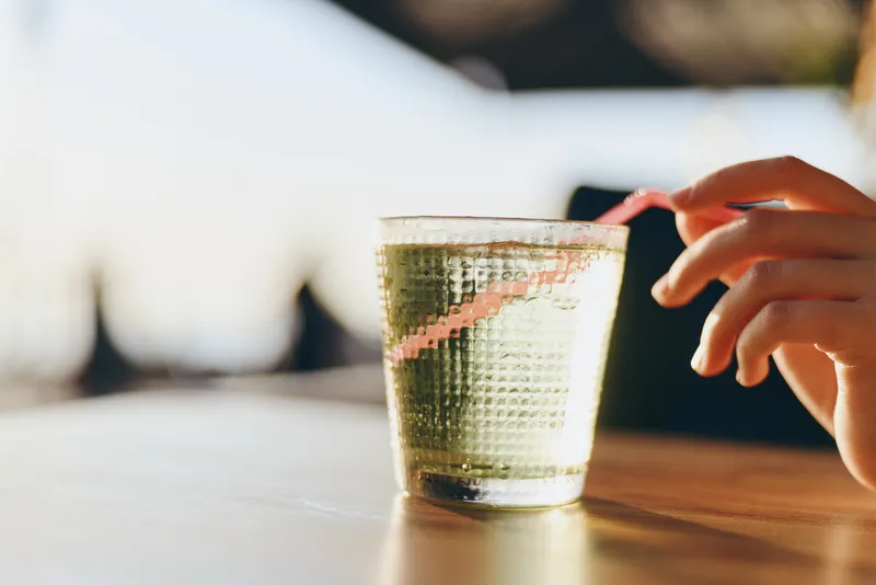 lifestyle woman in modern boho-western denim street style holding a glass with a straw, shot with warm film color tones and natural sunlight, casual vibe atmosphere