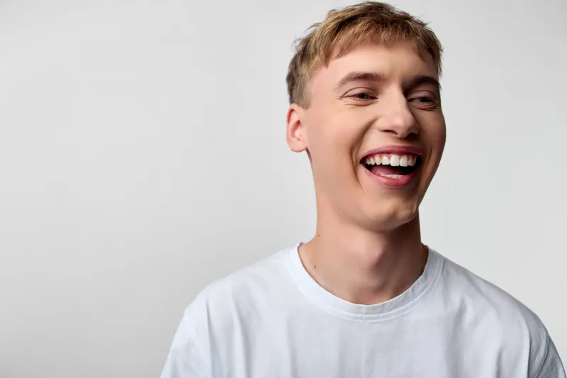Laughter and a bright smile from a casual, energetic man in a white shirt, capturing a candid, upbeat moment with authentic joy and relaxed mood in a studio setting