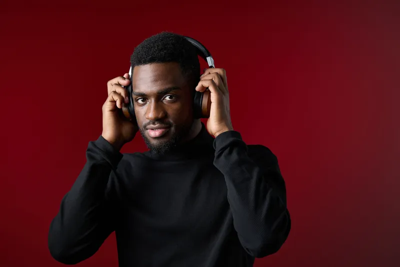 A stylish young Black man wearing headphones, with a confident expression against a vibrant red background, showcasing modern music and technology themes