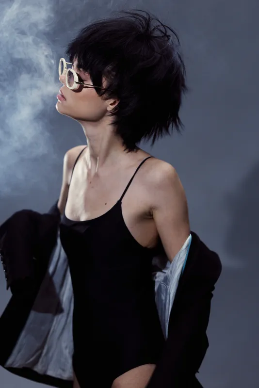 Stylish woman wearing sunglasses and black outfit posing with smoke background, edgy look, fashion concept.