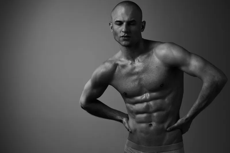 Black and white image of a muscular man posing confidently, showcasing his toned physique and athleticism, exuding strength and determination.