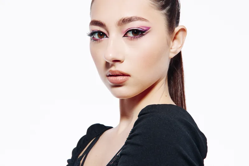 Close-up portrait of a young woman with creative pink eye makeup and flawless skin styling her hair back. Fashion concept with emphasis on beauty, elegance, and minimalistic background.