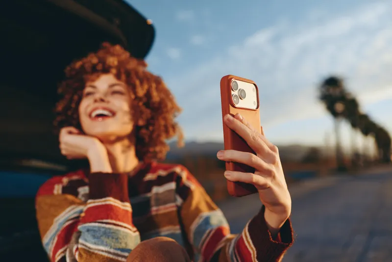Woman lifestyle selfie with smartphone outdoors on a city street, curly red haired woman smiling, holding phone up in candid travel moment, evening light, copy space