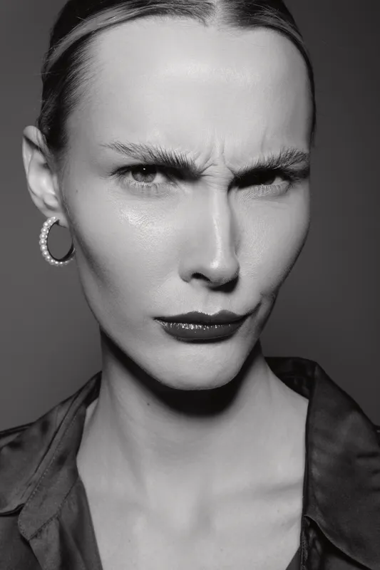 Close-up portrait of a serious white woman with pale skin and blonde hair wearing hoop earrings and dark lipstick. Concept for emotion, intensity, and fashion photography.