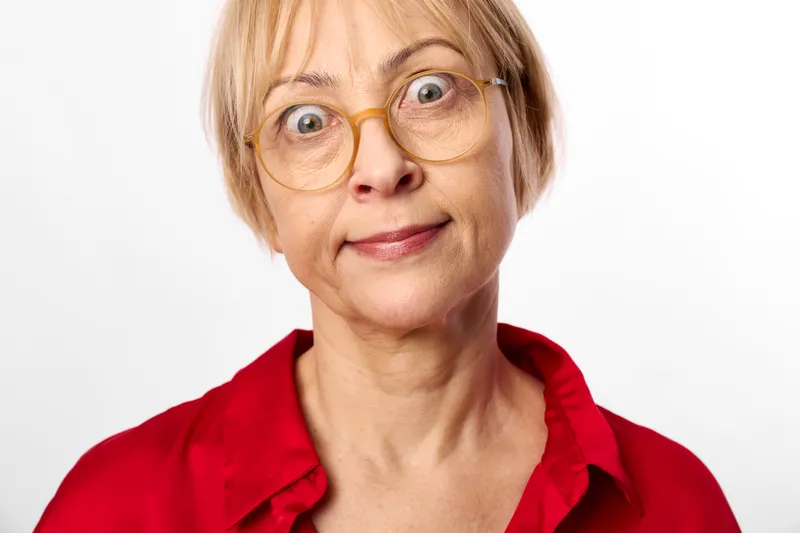 elderly woman portrait, glasses, surprised expression, closeup studio shot, blonde mature lady with round eyeglasses, looking at camera with wide eyes, isolated on white background