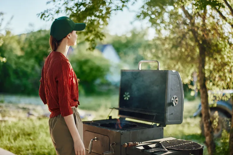 Young woman grilling outdoors in a casual outfit, enjoying a sunny day with a relaxed atmosphere in a green backyard Summer vibes with vibrant nature