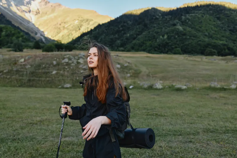 A solo photographer stands in a wide valley, camera ready with a long lens, preparing a shot among rolling hills and distant mountains in soft daylight.