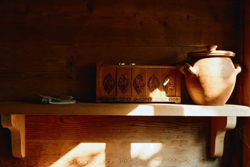 Shelf with wood texture, carved box and ceramic pot, warm sunlight creating shadows for rustic decor, storage feel and simple home textile mood inspiration for aesthetic