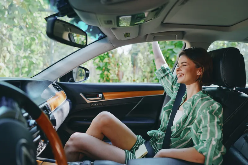 Cheerful woman driver sits in the car seat with a bright smile and hand on the steering wheel, ready for a joyful drive.