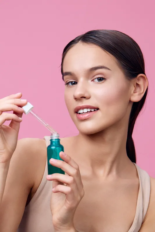 Young woman holding a serum bottle, smiling and promoting skincare with a pink background Skincare, beauty, health, cosmetic, model, vibrant, bright