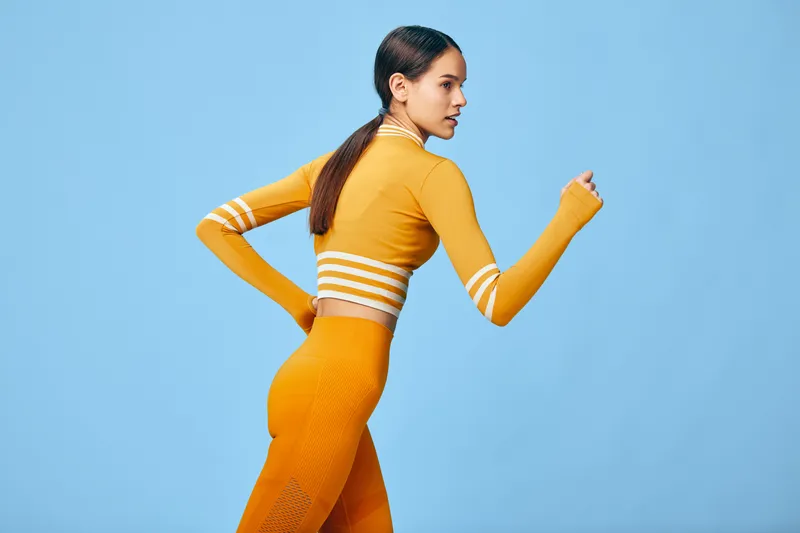 Female fitness athlete in a bright orange workout set runs in a studio with a clean blue background, showcasing motion, strength and energy for sport, training, and healthy lifestyle in everyday
