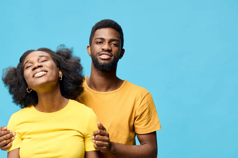 Happy young couple in matching yellow outfits smiling against a blue background, showcasing friendship and affection in a joyful moment