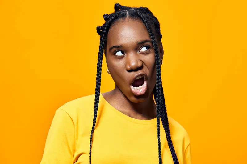 A playful young African woman with braids making a funny face against a vibrant yellow background, showcasing joy and spontaneity