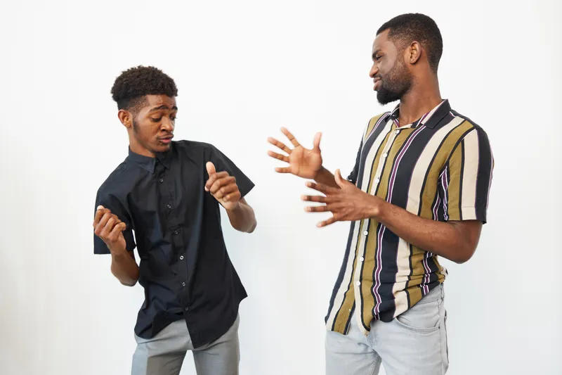 Two black men joyfully dancing together, expressing happiness and camaraderie in casual outfits. The vibrant colors of their shirts add to the lively atmosphere.