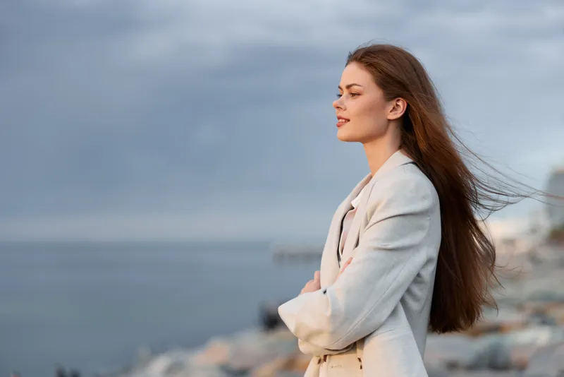 Confident woman in business attire enjoying a peaceful moment by the sea, showcasing elegance and professionalism against a serene backdrop.