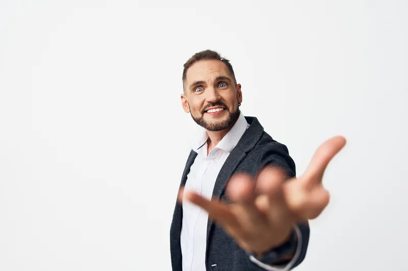 A confident business professional man extends a welcoming hand against a bright isolated colored background, radiating warmth, positivity, and openness.