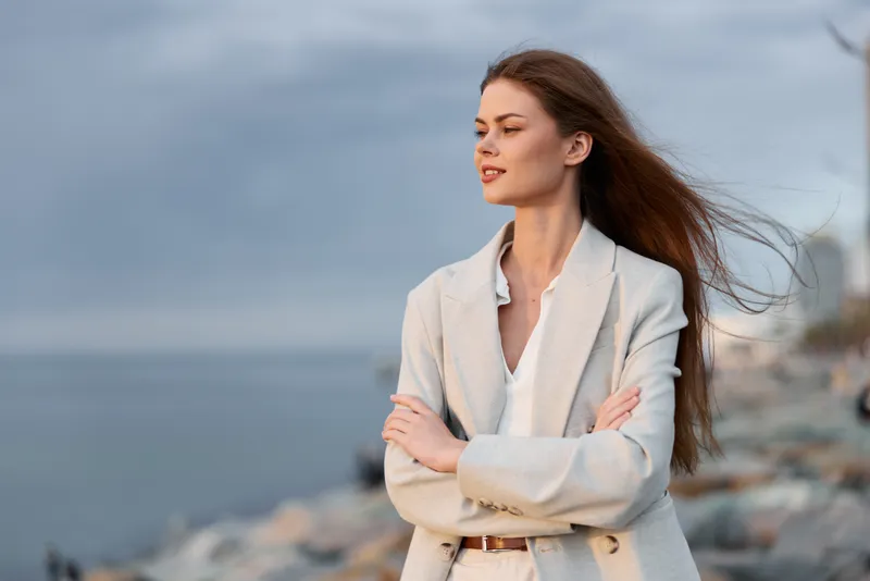 confident woman in beige blazer standing near sea coast with crossed arms natural light autumn business style KEY: confident woman, woman, businesswoman, autumn, beige blazer, crossed arms, natural li