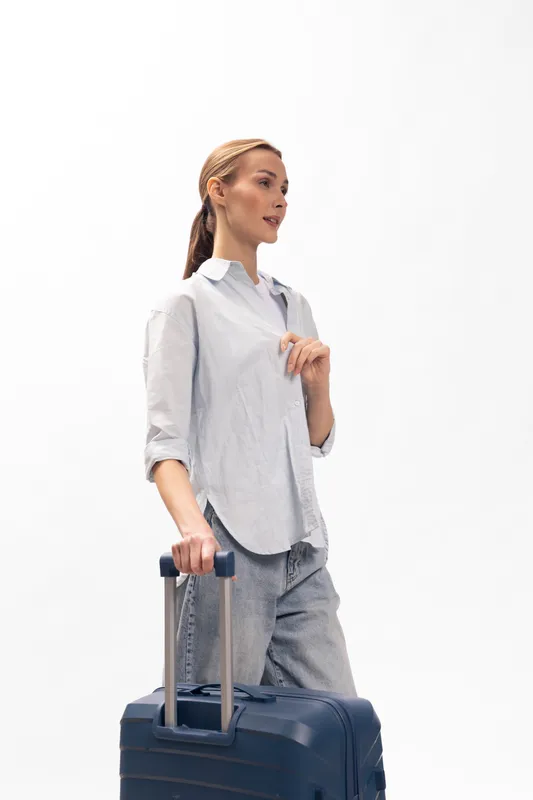 Young woman in casual clothes holding suitcase handle looks sideways isolated on white. Concept of travel, tourism, business trip and lifestyle for modern female traveler.