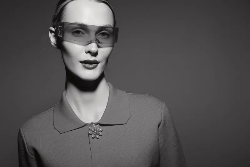 Portrait of a fair skinned Caucasian woman wearing transparent glasses and a textured outfit. Studio lighting creates a high contrast black and white fashion concept.