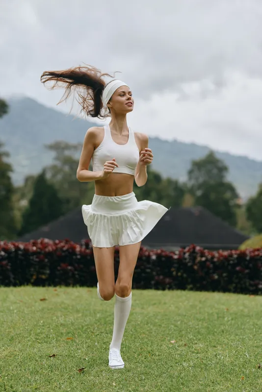 Young woman jogging in a sports outfit on a grassy field, portraying vitality and fitness in a natural, lush environment, evoking a sense of health and well being