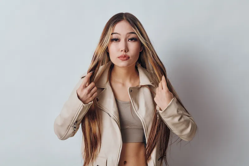 Young woman with long straight hair wearing beige jacket and crop top posing against white background, fashion, beauty and casual style portrait.