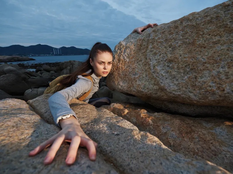 Young woman climbing on rocks, showing determination and strength against a seaside backdrop with a dramatic sky Adventure, resilience, nature exploration