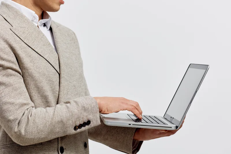 man working on laptop holding computer use digital nomad concept wearing beige jacket isolated light background
