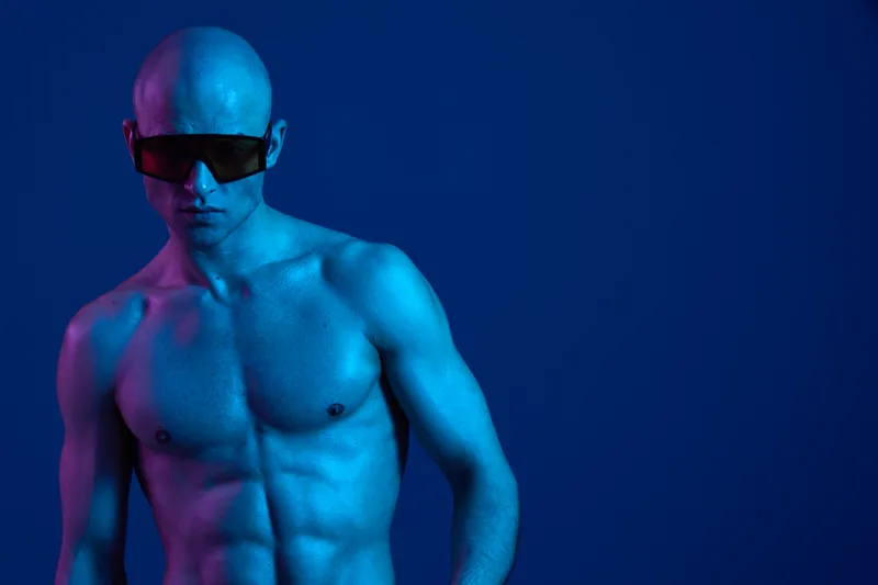 Bold man in sunglasses, featuring striking blue body paint and an eye-catching background, exuding a confident and modern aesthetic in this vibrant image.