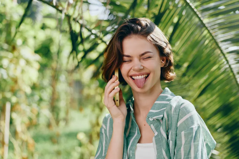 A cheerful woman talks on a mobile phone outdoors, enjoying a sunny moment.