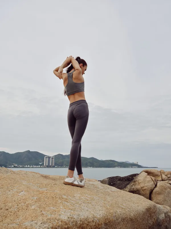 Young fit woman in sportswear stretching on the beach at sunrise, showcasing determination and fitness Gray activewear, coastal background, healthy lifestyle focus