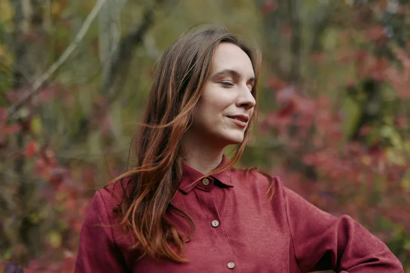 Close-up portrait of a young woman with a serene expression wearing a burgundy shirt, captured candidly outdoors to convey natural authenticity and quiet credibility in soft autumn light.