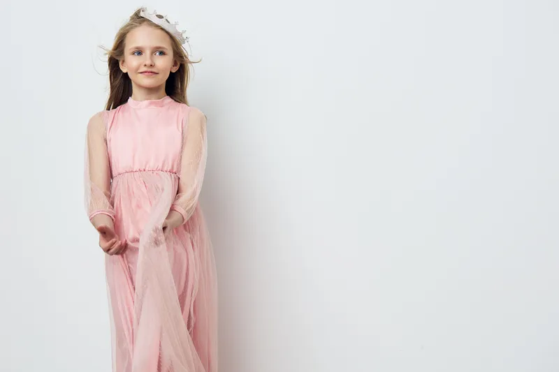 Young girl in a pink dress with a flower crown, exuding joy and innocence against a plain background, perfect for concepts of childhood and fashion