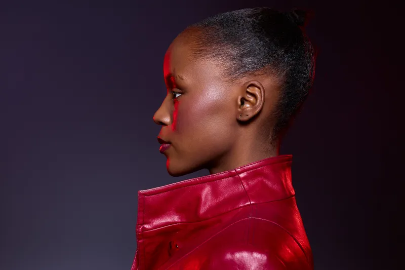 Profile of a young black woman with dark skin wearing a red leather jacket, posing against a dark purple background. Concept for fashion, beauty, and style with dramatic lighting.