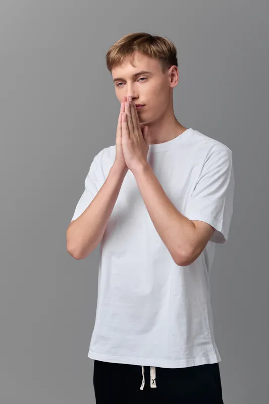 Prayer, contemplative man, hands in a thoughtful pose, casual white shirt in studio, depicting mindfulness, reflection, serenity and stillness as a calm moment of inner focus.