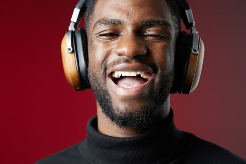 Happy young man enjoying music while wearing headphones, showcasing joy and relaxation against a vibrant red background