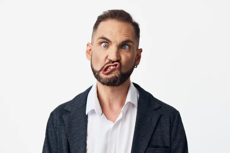 A professional business man stands against an isolated colored background, showing bold emotions and a quirky facial expression, conveying confidence, creativity, and dynamic mood.