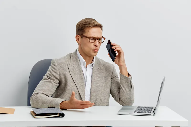 frustrated man using smartphone with laptop at table wearing glasses grey jacket white shirt cyber security concept