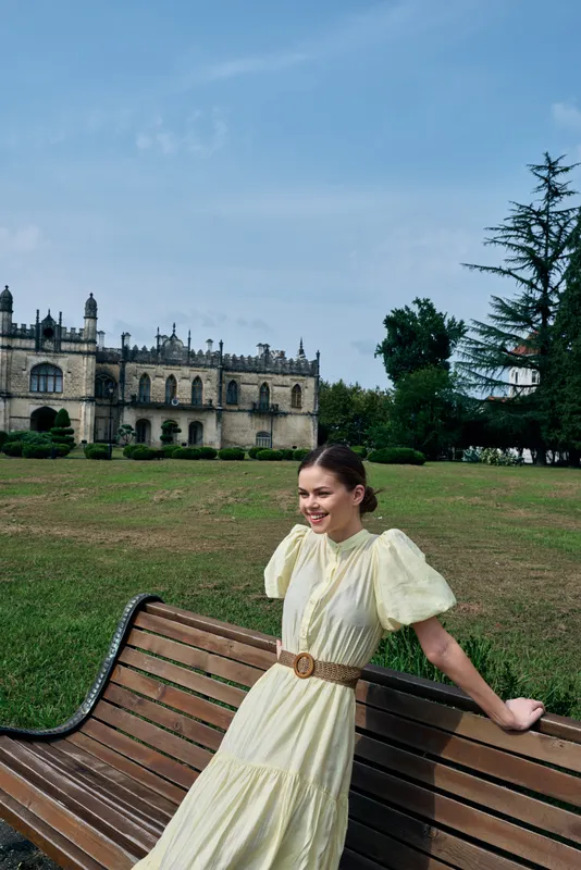 Woman on bench smile in park with historic building background wearing yellow dress outdoor showing authenticity and inclusivity
