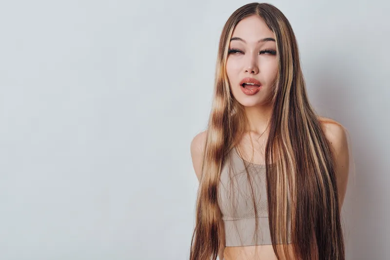 Portrait of young woman with long straight hair in casual top on light background with expressive face and eyes closed for fashion and beauty concept.