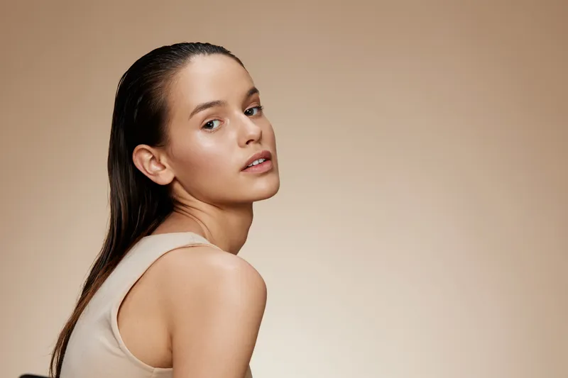 Elegant woman with wet hair in a natural makeup look, showcasing beauty and confidence against a soft beige background Perfect for skincare and beauty industries