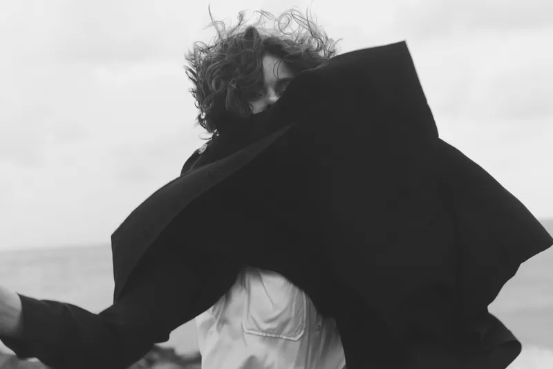 Motion, silhouette, fabric, wind, outdoor drama as a figure swirls a flowing cloak, creating mysterious movement, energy and tension in open air