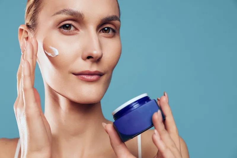 Cheerful skincare moment with a woman applying cream, facial moisturizer in hand, studio setting, natural tones, soft light, relaxed mood, clear skin glow, self care portrait