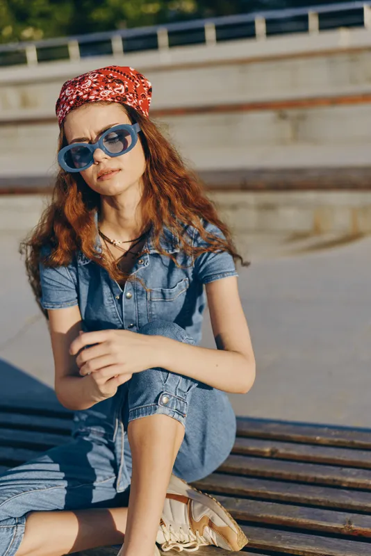 Lifestyle woman in modern boho-western denim street style wearing sunglasses and a red headscarf with natural sunlight and film color tones.