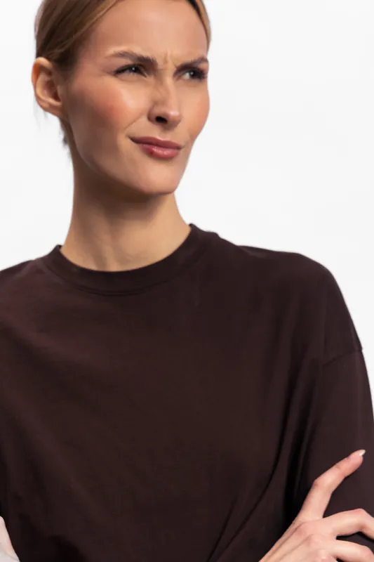 Confused young woman in dark sweater looks puzzled with furrowed brow and crossed arms. Isolated on white background. Concept for doubt, uncertainty, and skepticism.