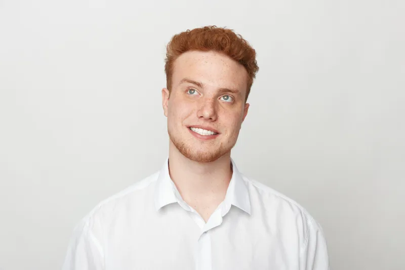 Smiling young man with red hair and beard wearing white shirt looks up thoughtfully on light background. Concept of positive emotions, hope, and casual lifestyle portrait.