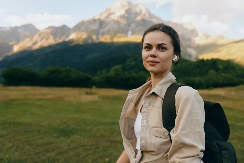 Casual woman with a backpack stands in a scenic countryside, enjoying outdoor life. Natural sunlight highlights landscape and adventure, creating a calm, hopeful mood.