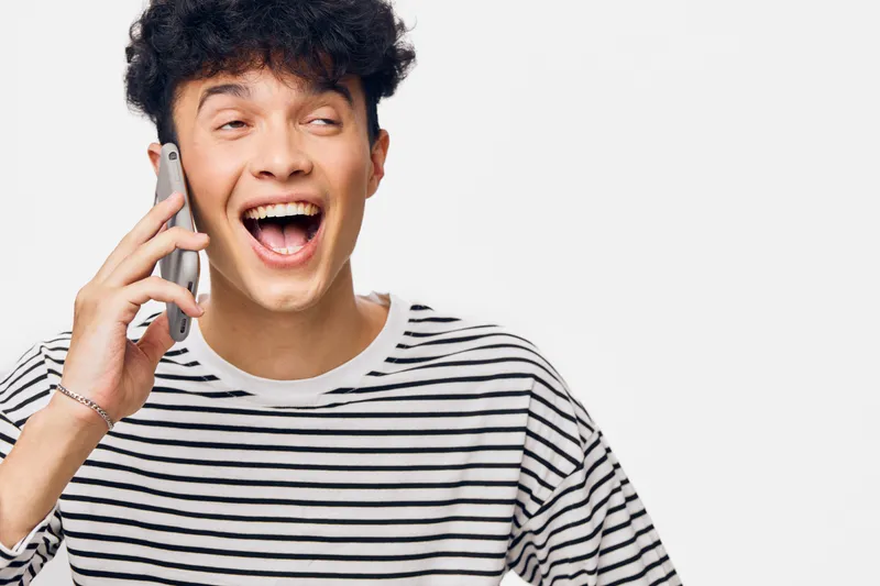 smiling man talking on smartphone wearing striped shirt, expressing joy and excitement in bright studio with white background