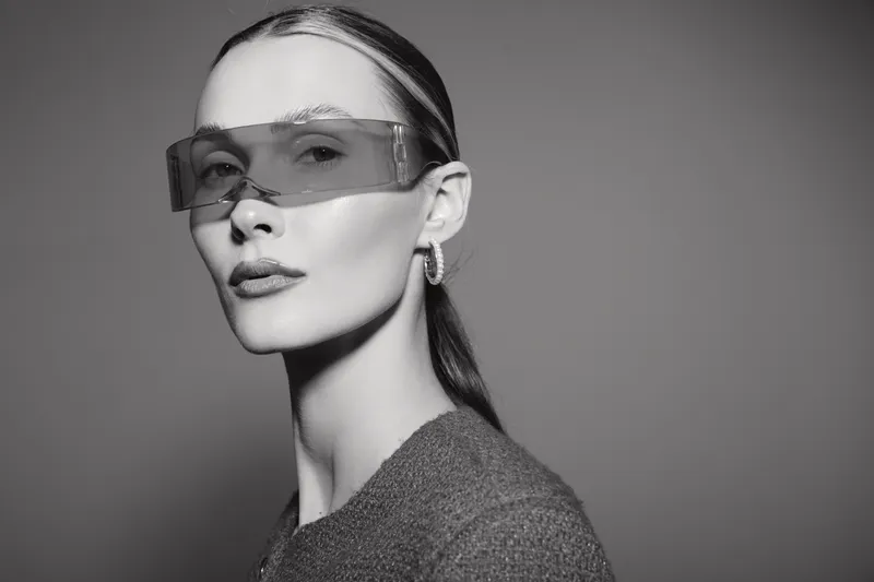 Blonde caucasian woman in grey sweater wearing large transparent glasses looking confident in studio. Concept of fashion and modern style.