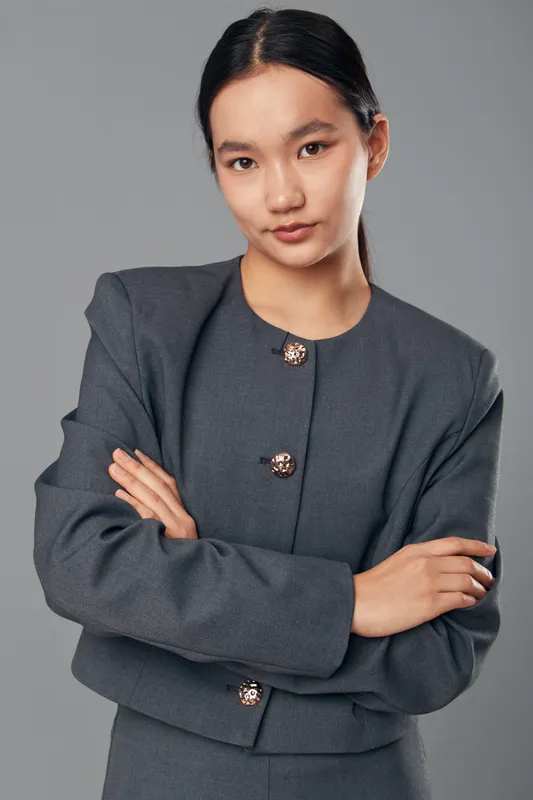 Young confident woman with crossed arms wearing stylish grey suit standing on grey background, portrait of professional businesswoman looking at camera with calm expression.