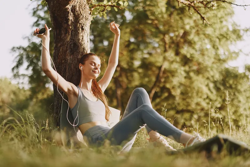 Happy young woman enjoying music outdoors in a park, wearing casual sportswear, expressing joy and relaxation in a vibrant nature setting